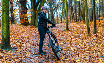 Beautiful middle-aged woman riding bicycle on path in forest in autumn. Side view	
