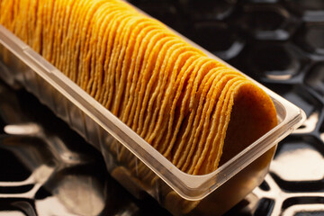 Potato chips arranged in a row in plastic packaging on a black baking tray