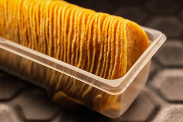 Potato chips arranged in a row in plastic packaging on a black baking tray
