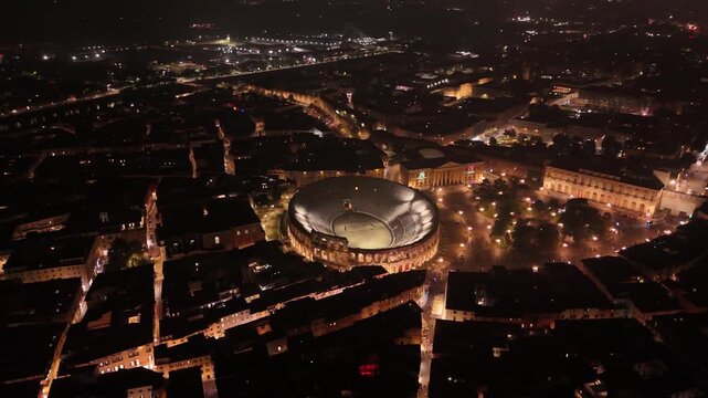 Majestic evening aerial of Verona with the illuminated Arena di Verona amphitheatre of 12 century, glowing city lights and historic streets creating a cinematic night atmosphere