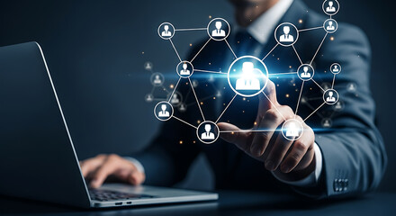 Businessman pointing at a network of people icons connected by lines while using a laptop, representing social media, human resources, and business connections.