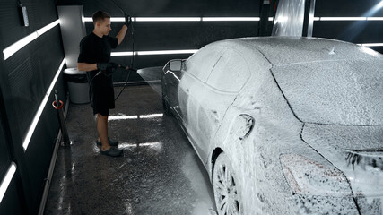Technician covering sedan with foam during car wash procedure. Concept of car care cleaning products, service marketing, corporate communication visuals.
