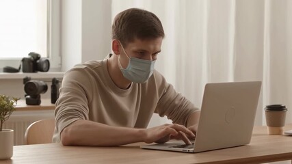 Young man wearing face mask working on laptop at home office - Powered by Adobe