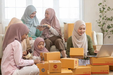 Muslim family running home based e-commerce business, packing boxes and using laptop together. Concept of teamwork, online selling, entrepreneurship and small family startup.