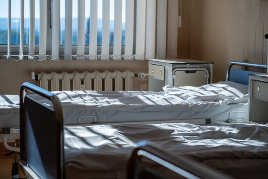 Multiple empty hospital beds with clean sheets lit by morning sunlight in ward - Powered by Adobe