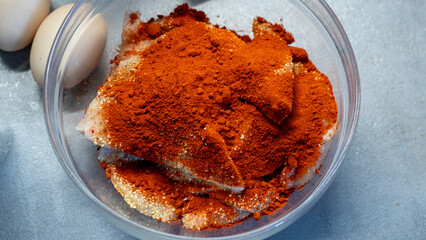 Raw chicken breast in bowl with paprika and seasoning, ready for cooking