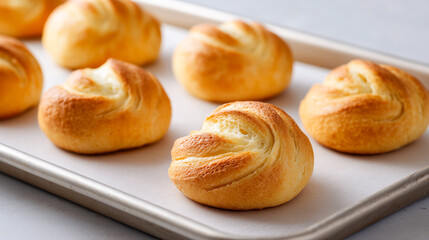 Fresh golden bread rolls cooling on a baking tray
