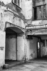 The corner of an old house with old iron pipes outside and a wall in a state of repair in black and white style