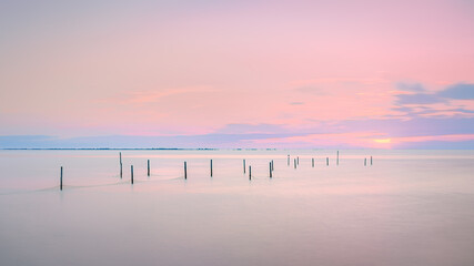 Vibrant sunset illuminates tranquil sea with leading lines of poles.