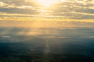 Beautiful sunrise scenery, rays of sunlight streaming through clouds on mountaintops and misty rice fields in rural Phayao, Northern Thailand.