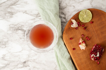 Pomegranate cocktail in sugar rimmed martini glass on white and gray marbled surface.