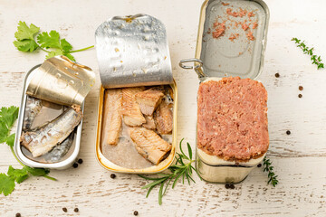 Three varieties of canned meat on a white, rustic table with spices and herbs.