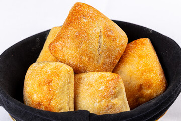 Five fresh, golden-crusted Ciabatta bread rolls served in a black fabric bread basket against a white tablecloth background.