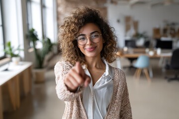 Amazed young Hispanic woman in casual attire with glasses presenting a pointing gesture toward the camera