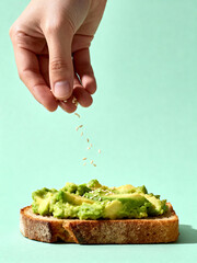 Female hand sprinkling guacamole on toast with sesame seeds
