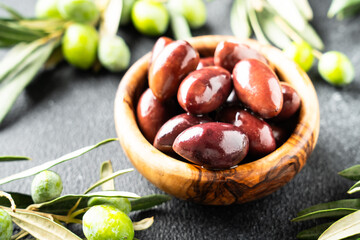 Olives in wooden bowl at black background.
