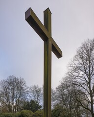 Large metal cross standing tall in cemetery under cloudy sky