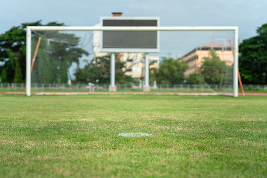 Football field with green grass ground, selective focus at penalty kick point as foreground and goal as blurred background. 