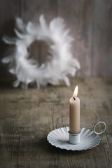 Eine brennende Kerze in einem Kerzenhalter und ein wei&szlig;er Kranz im Hintergrund. Weihnachten, rustikaler Stil.