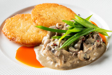 Crispy golden potato pancakes (draniki, latkes, rosti) topped with creamy mushroom sauce and fresh green onions on a white plate