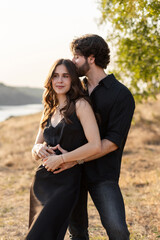 Young couple standing in warm sunset light, romantic outdoor portrait with tender embrace