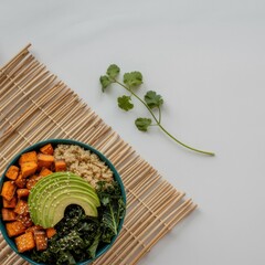 Healthy vegan power bowl with sweet potatoes, quinoa, kale, and avocado on a bamboo mat