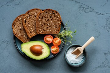Healthy breakfast ingredients with dark bread avocado cherry tomatoes and salt on a plate