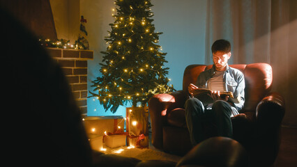 Man Reading a Book While Sitting on the Sofa at Christmas Near the Tree