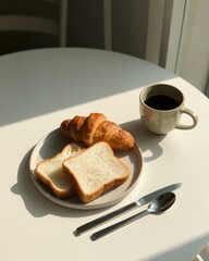 Morning breakfast with a croissant, two slices of bread, and a cup of coffee on a white table