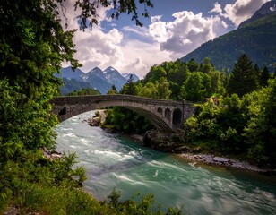 A stone arch bridge spans a turquoise river amidst lush greenery and distant snow-capped mountains under a cloudy sky