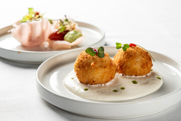 Gourmet arancini appetizers on a white plate with creamy sauce, herbs, and soft background bokeh. Upscale restaurant dining food photography