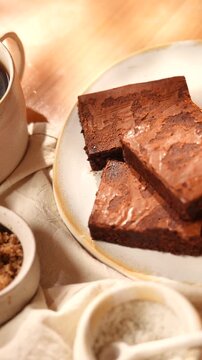 Three brownies are stacked on a white plate. A cup of coffee is sitting next to the plate
