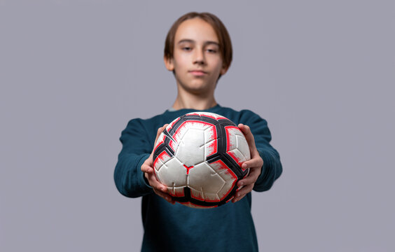 Boy holding a soccer ball on a gray background. Sports and children concept. Portrait smiling young boy kids holding a soccer ball, fullball. Cute child playing football sport hobby for kids