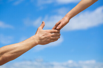 Hands of man and woman reaching to each other, support. Giving a helping hand. Hands of man and woman on blue sky background. Lending a helping hand. Solidarity, compassion, and charity, rescue
