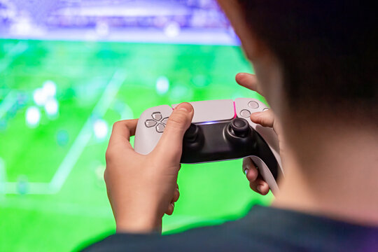 Playing football video game at home. Boy addicted to playing video games. Gamer holds a joystick in his hands, plays a video game on a large TV screen friends. Joystick, computer monitor. Video game