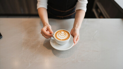 Barista's Hands Presenting Latte Art Coffee Cup on Marble Countertop