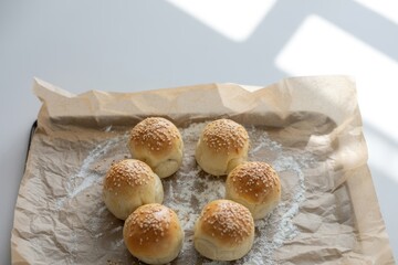 Six freshly baked sesame seed bread rolls arranged in a circle on parchment paper