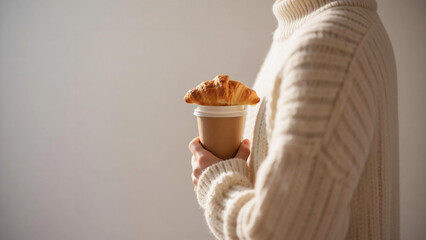 Croissant atop coffee cup held by person in cozy white sweater