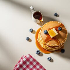 Stack of golden pancakes with blueberries butter and maple syrup pouring from a pitcher