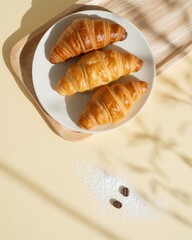 Three freshly baked golden croissants served on a white plate with coffee beans and sugar