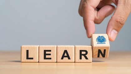 Wooden blocks spelling "LEARN" with hand holding final block on gray background.
