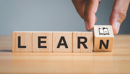 Wooden blocks spelling "LEARN" with hand holding final block on gray background.