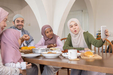 Happy Muslim family enjoying meal together at home while using digital tablet. Concept of Ramadan, Islamic family bonding, multicultural lifestyle and digital connection over food.