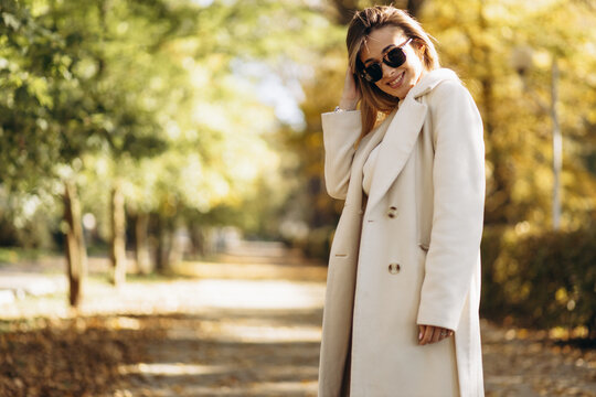 Young woman wearing coat and sunglasses walking in an autumn park