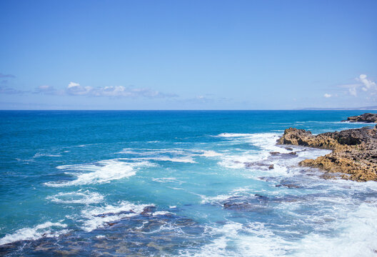 Serene coastal landscape with turquoise waters gently lapping against rocky shorelines under a clear blue sky, creating a tranquil and picturesque natural scene - Powered by Adobe