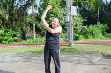 Mature Asian Woman Stretching Arm in Green Park for Health and Wellness
