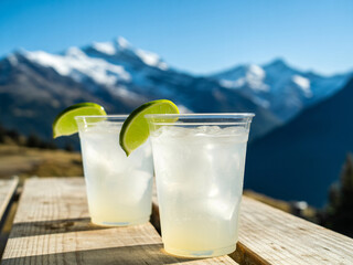 Crisp, refreshing lime drinks with ice sit on a wooden table against a stunning mountain vista, perfect for outdoor relaxation and enjoyment.