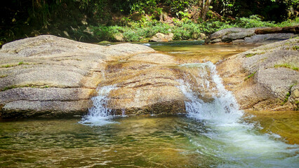 Small Waterfall Cascading Over Smooth Granite Rocks in a Vibrant Tropical Forest Stream