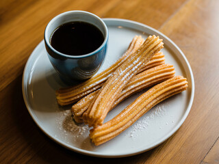 Indulge in warm, golden churros dusted with powdered sugar, perfectly paired with a rich cup of dark coffee for a delightful morning treat.