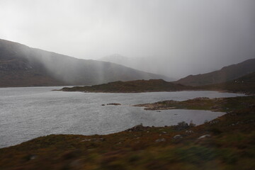 Scottish mountain loch in autumn surrounded by mountain peaks and rugged slopes, with water reflecting the dramatic highland landscape in Scotland